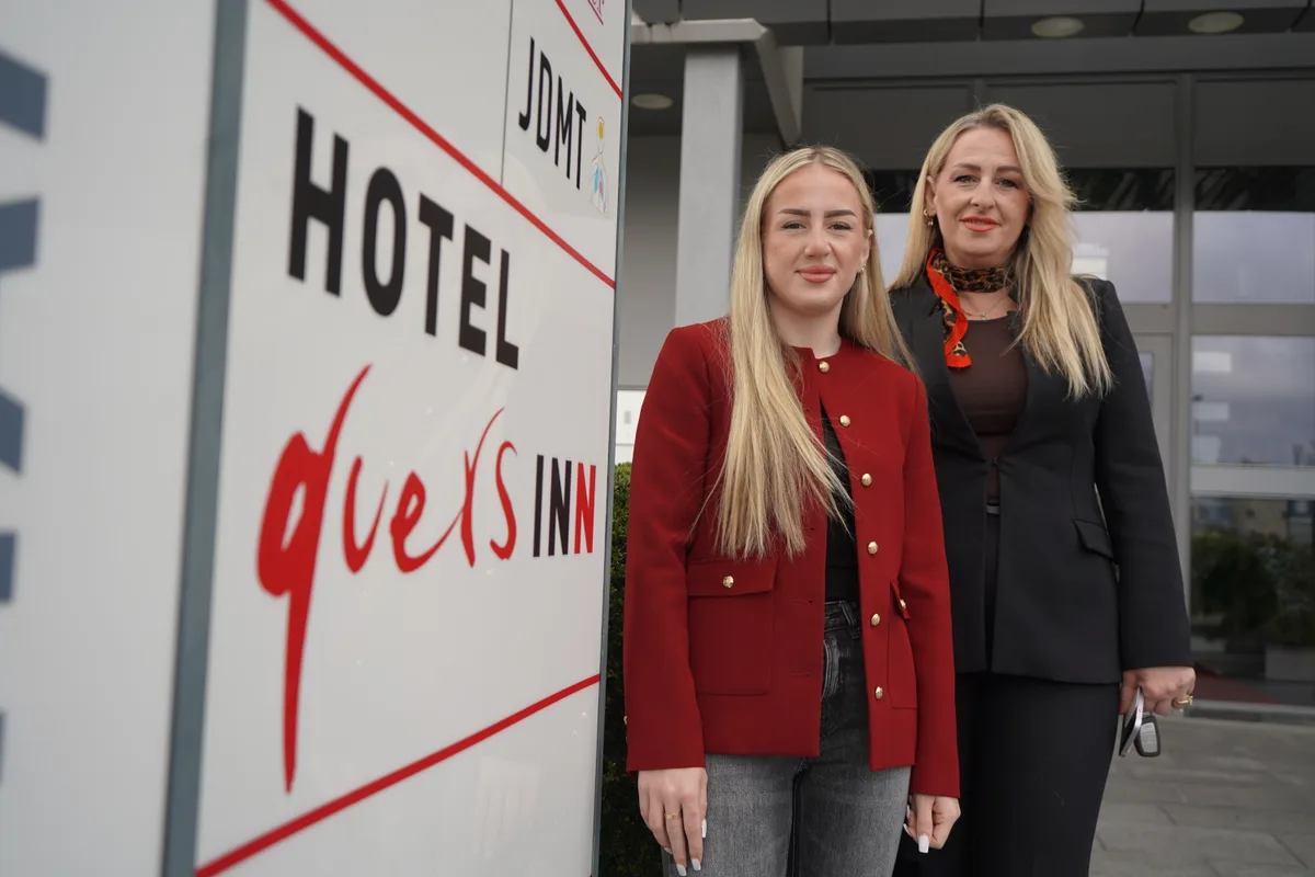 Eine junge Frau und ihre Mutter stehen neben einer Stele, auf der Quers Inn steht.